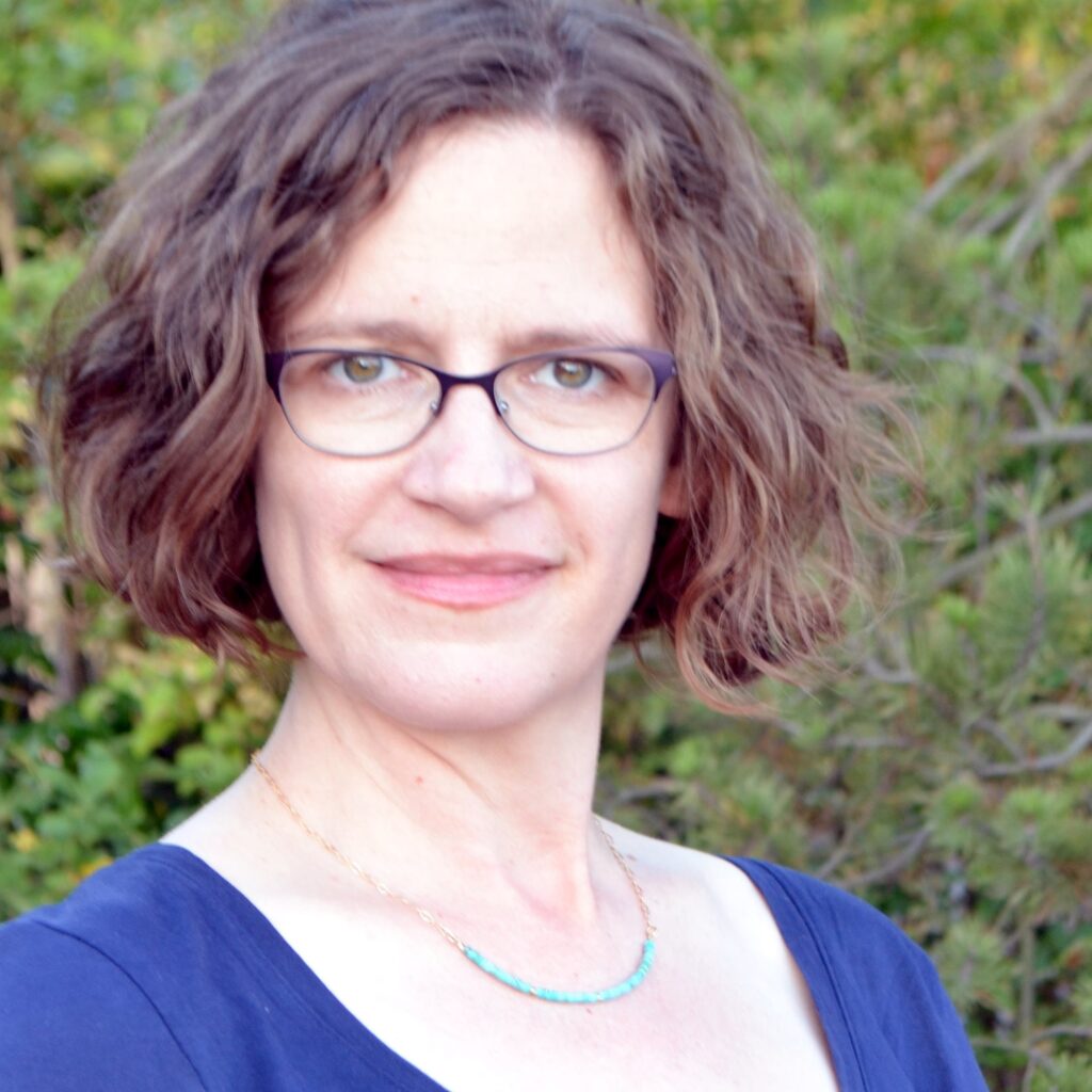 Photo of a white woman wearing a blue shirt and glasses.